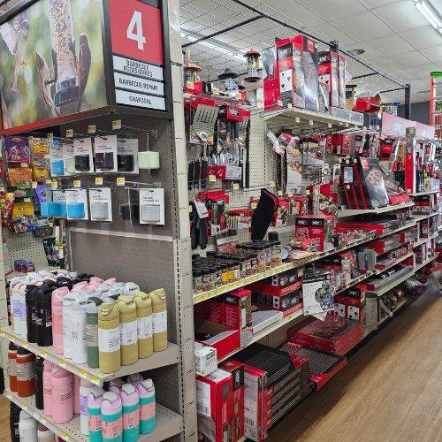 Store aisle filled with barbecue and grilling supplies. Products include utensils, sauces, and colorful water bottles. Bright, organized, inviting.