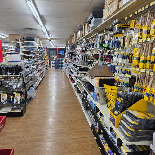 A brightly lit hardware store aisle with shelves filled with tools and supplies. The orderly display and wooden floor create a tidy, inviting atmosphere.