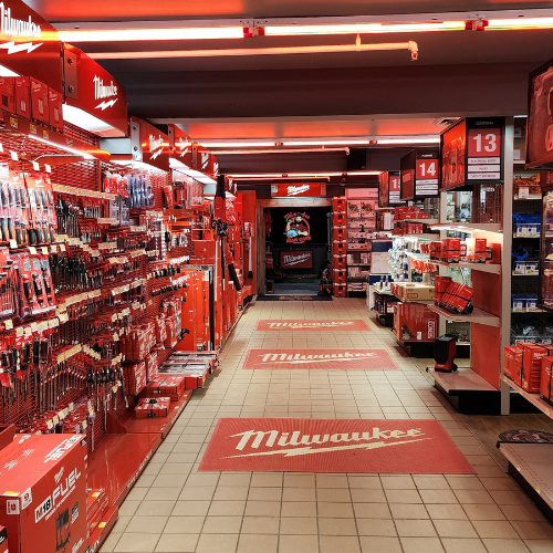 A well-organized man cave features an array of neatly displayed red Milwaukee power tools on shelves. The setting is enhanced by a branded sign and a cozy, focused ambiance.