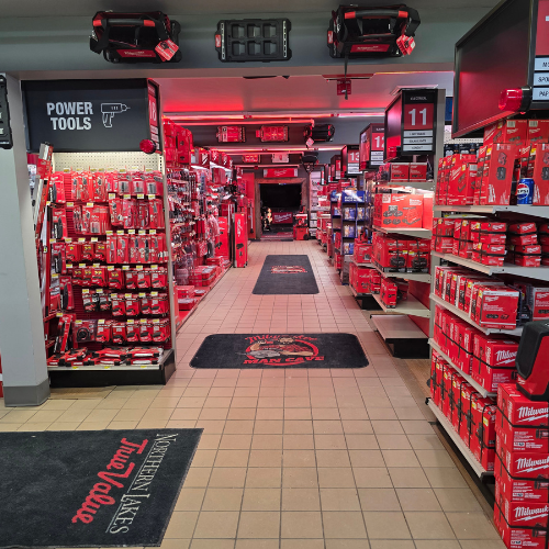 A store aisle filled with red Milwaukee tool boxes, bags, tools and storage units. Bright lighting reflects off the red decor, creating a vibrant, energetic atmosphere.