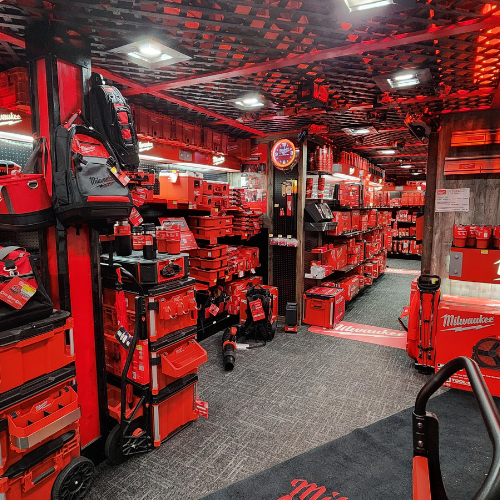 A well-organized man cave features an array of neatly displayed red Milwaukee power tools on shelves. The setting is enhanced by a branded sign and a cozy, focused ambiance.