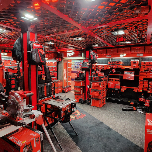A well-organized man cave features an array of neatly displayed red Milwaukee power tools on shelves. The setting is enhanced by a branded sign and a cozy, focused ambiance.