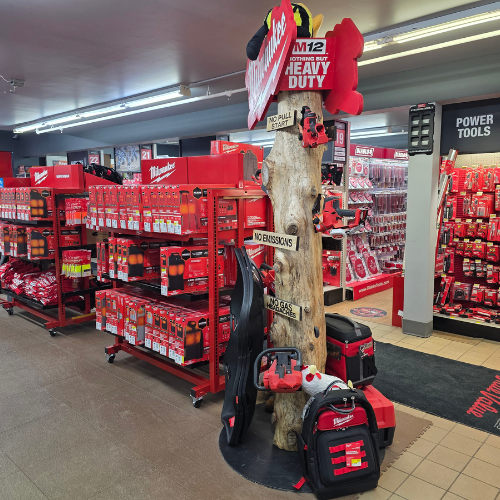 A store aisle filled with red Milwaukee tool boxes, bags, tools and storage units. Bright lighting reflects off the red decor, creating a vibrant, energetic atmosphere.