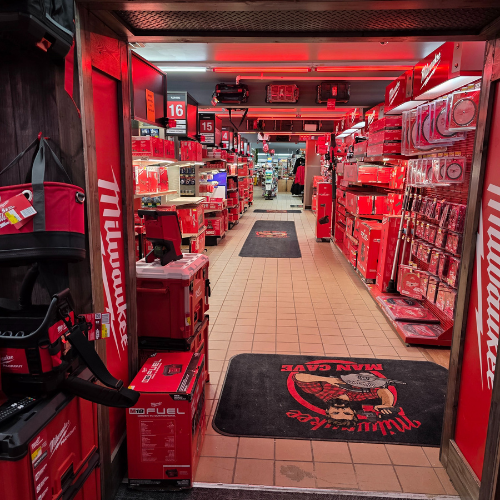 A store aisle filled with red Milwaukee tool boxes, bags, and storage units. Bright lighting reflects off the red decor, creating a vibrant, energetic atmosphere.