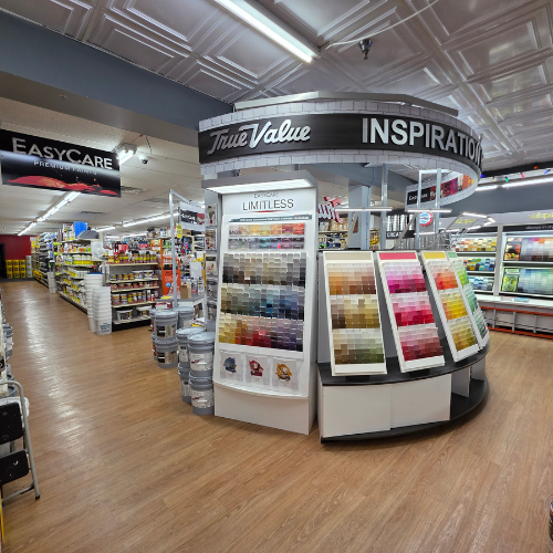 A hardware store interior with wooden flooring, displaying a central color swatch stand labeled 