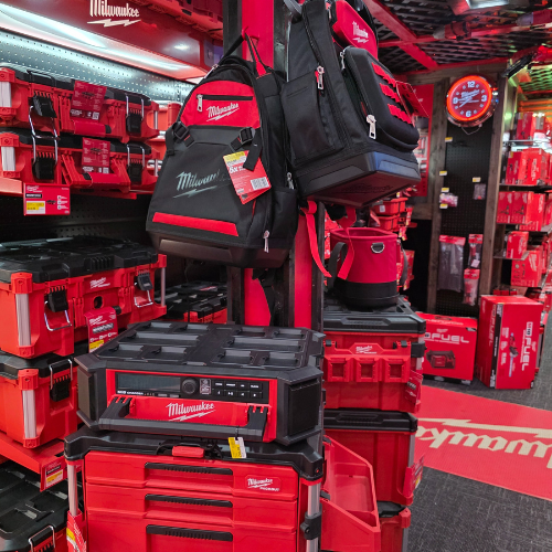 A store aisle filled with red Milwaukee tool boxes, bags, and storage units. Bright lighting reflects off the red decor, creating a vibrant, energetic atmosphere.