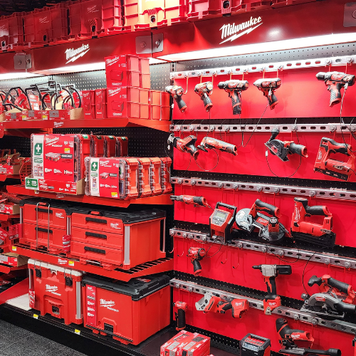 A well-organized man cave features an array of neatly displayed red Milwaukee power tools on shelves. The setting is enhanced by a branded sign and a cozy, focused ambiance.