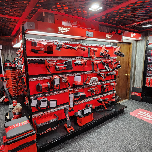 A well-organized man cave features an array of neatly displayed red Milwaukee power tools on shelves. The setting is enhanced by a branded sign and a cozy, focused ambiance.