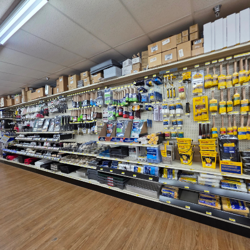 A well-organized hardware store aisle displays painting supplies, brushes, rollers, and tools neatly on shelves. Bright lighting and wood flooring set a tidy, inviting tone.