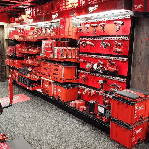 A well-organized man cave features an array of neatly displayed red Milwaukee power tools on shelves. The setting is enhanced by a branded sign and a cozy, focused ambiance.