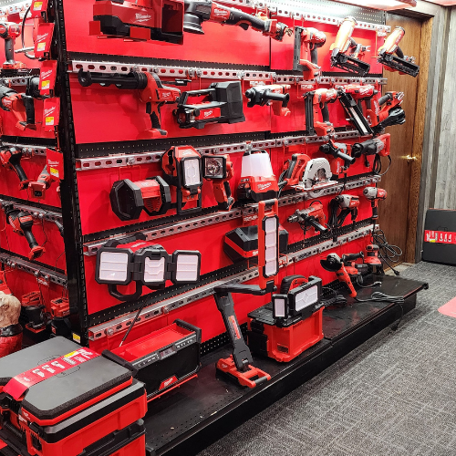 A well-organized man cave features an array of neatly displayed red Milwaukee power tools on shelves. The setting is enhanced by a branded sign and a cozy, focused ambiance.