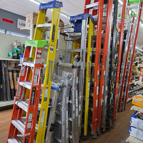 A variety of ladders in orange, yellow, and silver are displayed upright in a hardware store aisle, creating a colorful and organized scene.