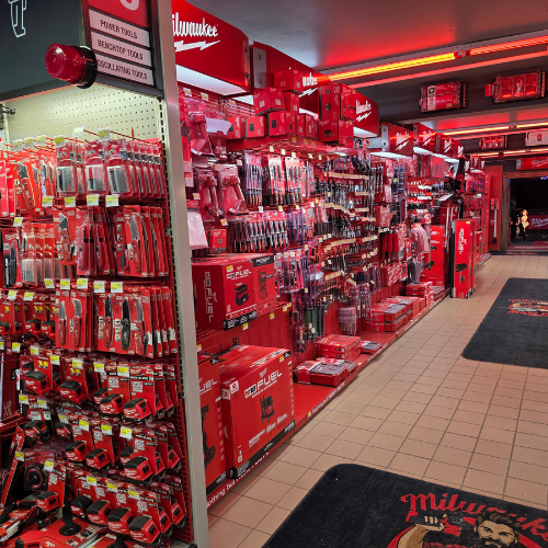A store aisle filled with red Milwaukee tool boxes, bags, tools and storage units. Bright lighting reflects off the red decor, creating a vibrant, energetic atmosphere.