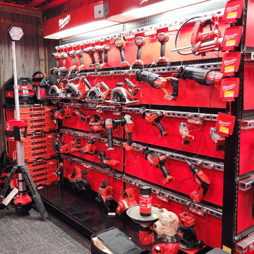A well-organized man cave features an array of neatly displayed red Milwaukee power tools on shelves. The setting is enhanced by a branded sign and a cozy, focused ambiance.