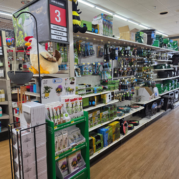 A store aisle displays various gardening tools and outdoor supplies. Items are neatly organized on shelves, creating a vibrant and busy atmosphere.