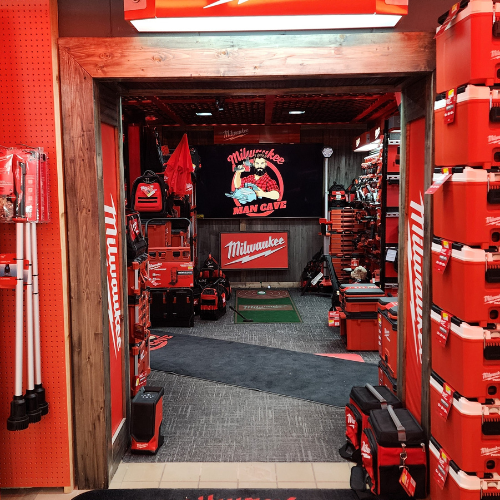 A well-organized man cave features an array of neatly displayed red Milwaukee power tools on shelves. The setting is enhanced by a branded sign and a cozy, focused ambiance.