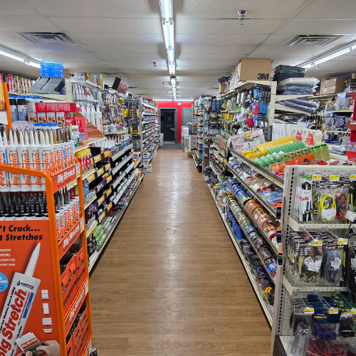 A well-lit hardware store aisle lined with various tools and supplies, including adhesives and tapes. The shelves are neatly organized, creating a welcoming atmosphere.