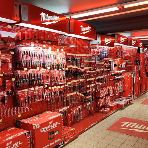 A well-organized man cave features an array of neatly displayed red Milwaukee power tools on shelves. The setting is enhanced by a branded sign and a cozy, focused ambiance.