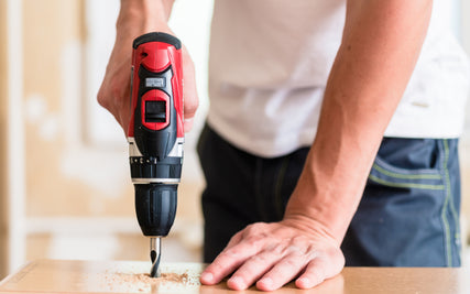 Power Tool RentalsA person using a red cordless drill to make a hole in a wooden surface, with sawdust scattered. The image conveys focus and precision in DIY work.
